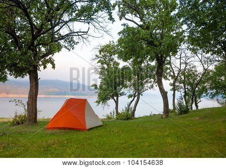 Orabge camping tent on a river shore in a morning light