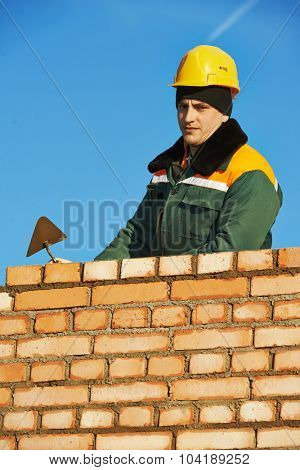 construction mason worker bricklayer installing red brick with trowel putty knife outdoors