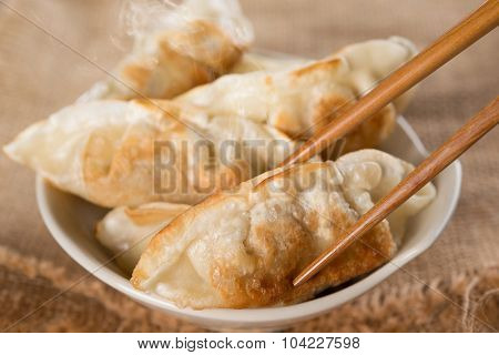 Close up fresh pan fried dumplings on bowl with chopsticks and hot steams. Asian food on rustic vintage wooden background.