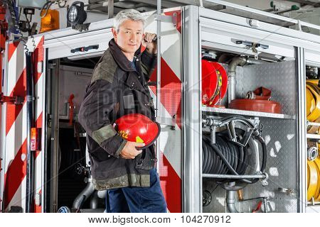 Portrait of confident fireman in uniform standing on fire engine at station