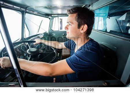 Side view of young male firefighter driving truck at fire station