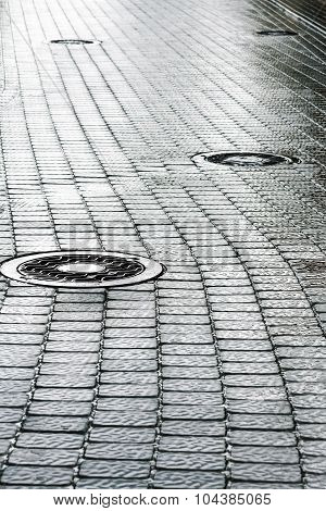 Sewer Manhole On Wet Cobblestone Street
