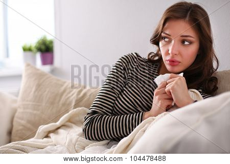 Portrait of a sick woman blowing her nose while sitting on the sofa