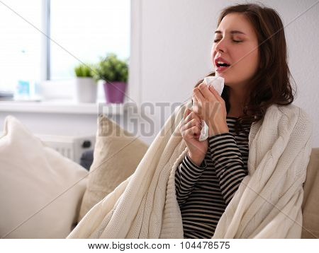 Portrait of a sick woman blowing her nose while sitting on the sofa