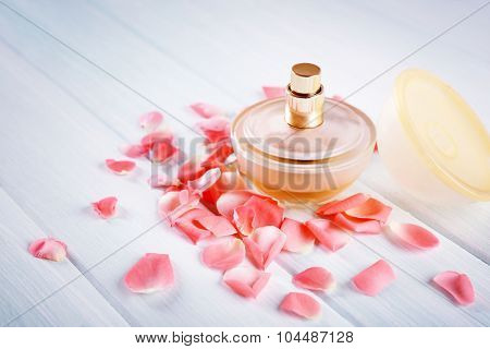 Bottle of perfume and flowers petals on wooden background