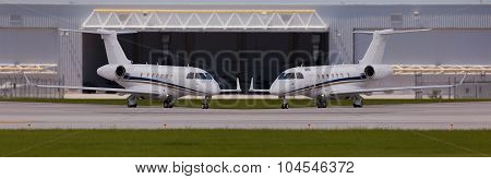 Two private planes in front of a hangar