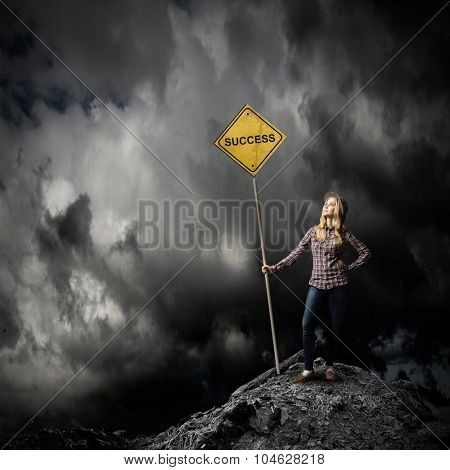 Young woman satnding on rock top with signboard