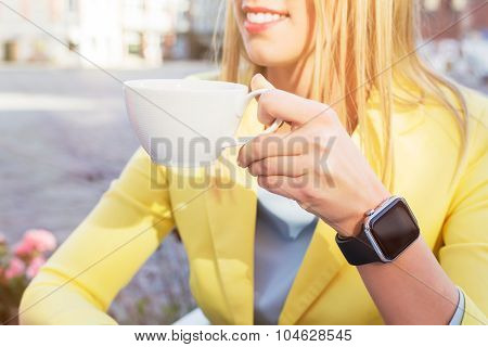 Woman with a smartwatch around her wrist holding a cup of coffee
