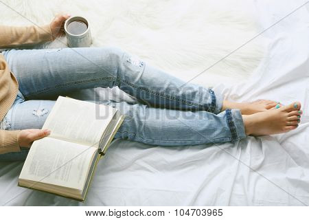 Woman on the bed with old book and cup of coffee, top view point