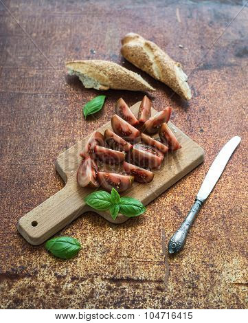 Ripe kumato tomatoes, basil leaves and knife on a rustic wooden chopping board over grunge rusty met