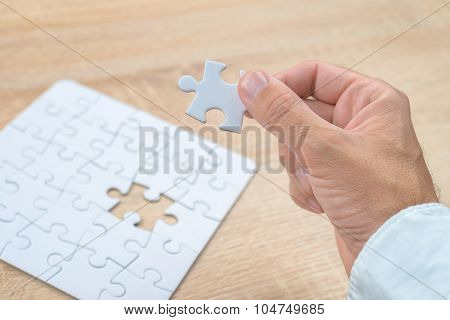 Businessman Hand Putting A Missing Piece Into Jigsaw Puzzle