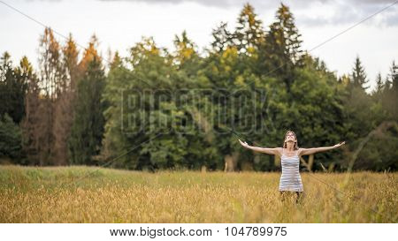 Young Woman Standing In The Middle Of Autumn Meadow With High Golden Grass