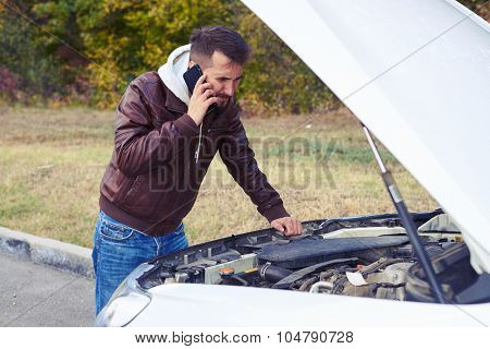discontented man talking on the phone and looking under the hood of breakdown car at outdoor