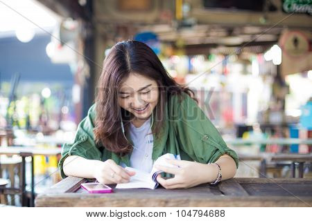Charming Asian Girl Sitting By Wooden Table And Reading Book