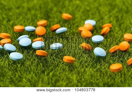 Scattered orange and blue round pills on the green grass
