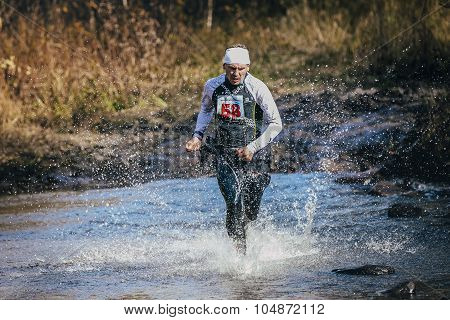 runner middle-aged man crossing river, and around him water splashes