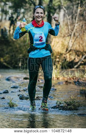 young woman runner smiling while crossing a mountain river