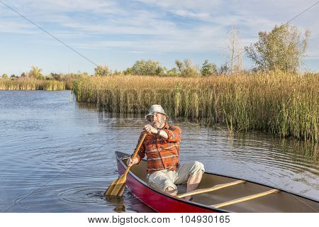 senior paddler enjoying paddling a red canoe on a calm lake, Riverbend Ponds Natural Area, Fort Collins, Colorado