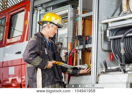Side view of male firefighter fixing water hose in truck at fire station