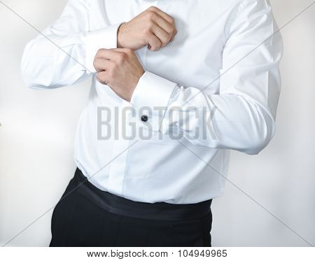 A groom putting on cuff-links as he gets dressed in formal wear