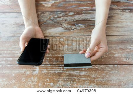 business, technology, cash free and internet people concept - close up of male hands holding smart phone and credit card on wooden table