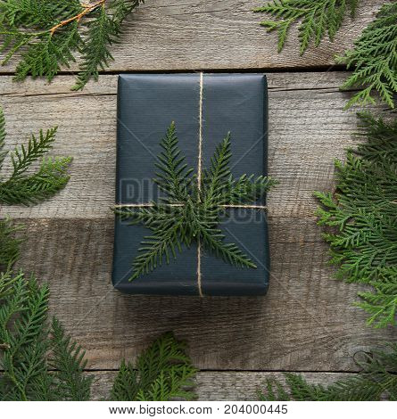 Christmas gift box wrapped in black paper with snowflakes around branch cypress on wooden surface.