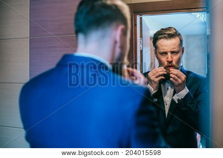 Handsome stylish groom with beard and mustache getting dressed and preparing for the wedding day.