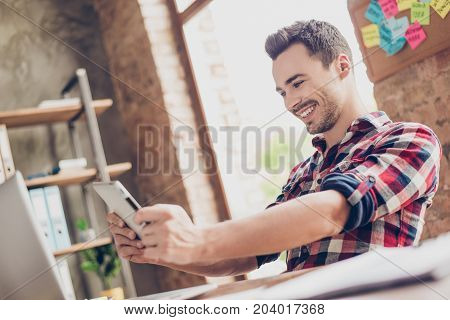 Cheerful Young Brunet Attractive Hipster Worker Is Plying A Game On His Tablet In Office. He Is Very
