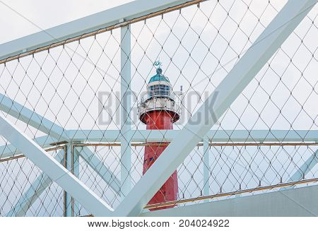 The lighthouse of Scheveningen in Netherlandsseen through the gauze of a bicycle bridge