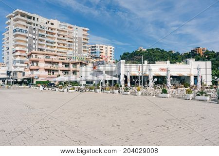ALBANIA DURRES - September 22 2015: Quay of the city of Durres with cafes which have tables and umbrellas from the sun in the background green hills and residential complex.