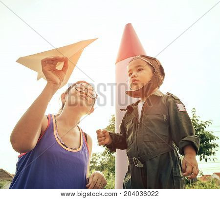 mother with paper plane in hand playing with son wearing military pilot suit in garden