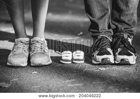 Waiting of baby. Little booties sneakers near the feet of my father and mother. Pregnant woman pregnancy motherhood. Happy family. Mom's Dad's and baby's bootees. Family look. black and white photo
