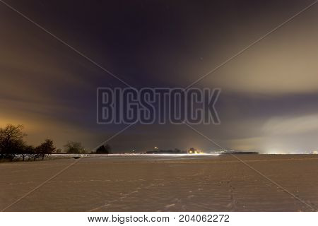 View over a wide snow covered field with a distant street at night. Taken in Lachen-Speyerdorf in Rhineland-Palatinate, Germany