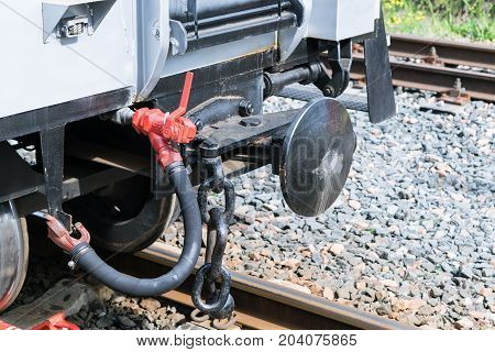 Drawbar railway car with an air hose and chain. Rails with concrete sleepers. In the background the rails and gravel. Convex coupling circle. Rail car gray. Day the sun is shining.