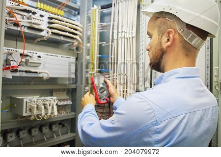 Engineer electric with multimeter. Side view of male technician examining fusebox with multimeter probe