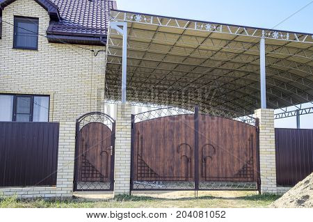 Brick House With A Fence And Gates. A Large Awning With A Steel Frame. View Of A New Built-up Fence