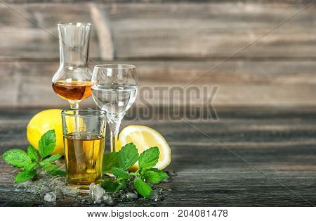 Alcoholic drinks with ice lemon mint leaves on wooden background. Aperitif whiskey gin rum vodka