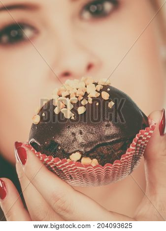 Diet sweets food concept. Woman holding delicious chocolate cupcake with peanut frosting about to take bite
