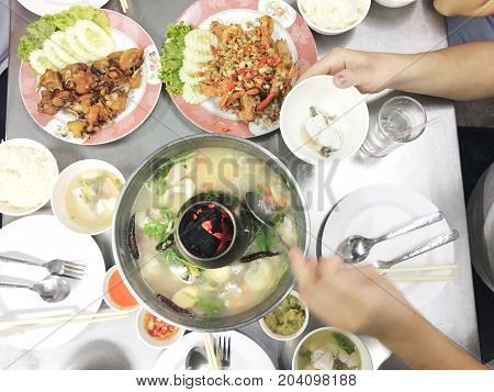 Woman Hands Holding A Mug Of Tom Yam Mixed Sea Food With Mushroom In Hot Pot With Family Dinner On T