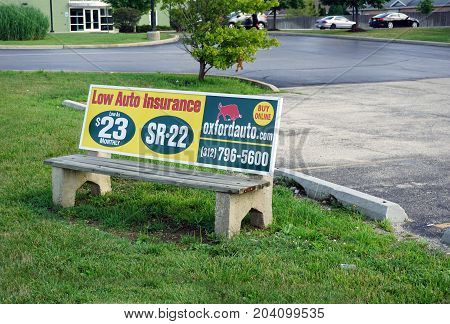 CREST HILL, ILLINOIS / UNITED STATES - JULY 20, 2017: An advertisement on a bench, at a bus stop on Plainfield Road, advertises low auto insurance.