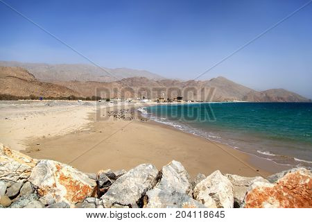 View on a dirty beach in Oman sunny hot day Al Hajar Mountains at the background no people