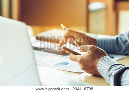 Busnessman Looking Data Information On Smart Phone About Stock Marketing And Calculate On Desk In Of