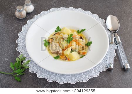 Creamy soup with fish fillet and mussels in a white plate on a white cloth on a grey abstract background. Healthy eating concept. Mediterranean lifestyle