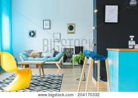 Modern designer barstool at blue kitchen island in colorful living room with yellow chair