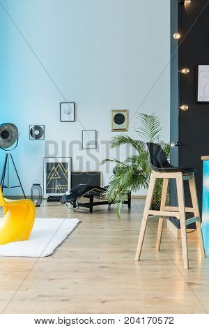 Designer eclectic loft with barstool lamp and posters on white wall and wooden floor