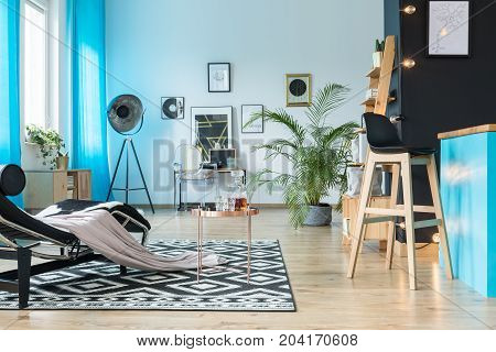 Barstool in cozy open space with copper table and chaise lounge on geometric carpet