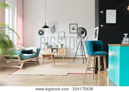 Blue barstool in kitchen area in warm room with turquoise settee with pillows and table on carpet