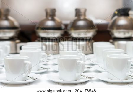 Many rows of white coffee cup with saucer and teaspoon on table and coffee maker background