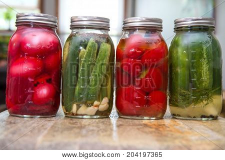 Row of homemade rustic organic pickled beet eggs cucumbers and cherry peppers