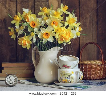 Bouquet of yellow daffodils in a white jug. Still life in rustic style with flowers alarm clock and kitchenware.